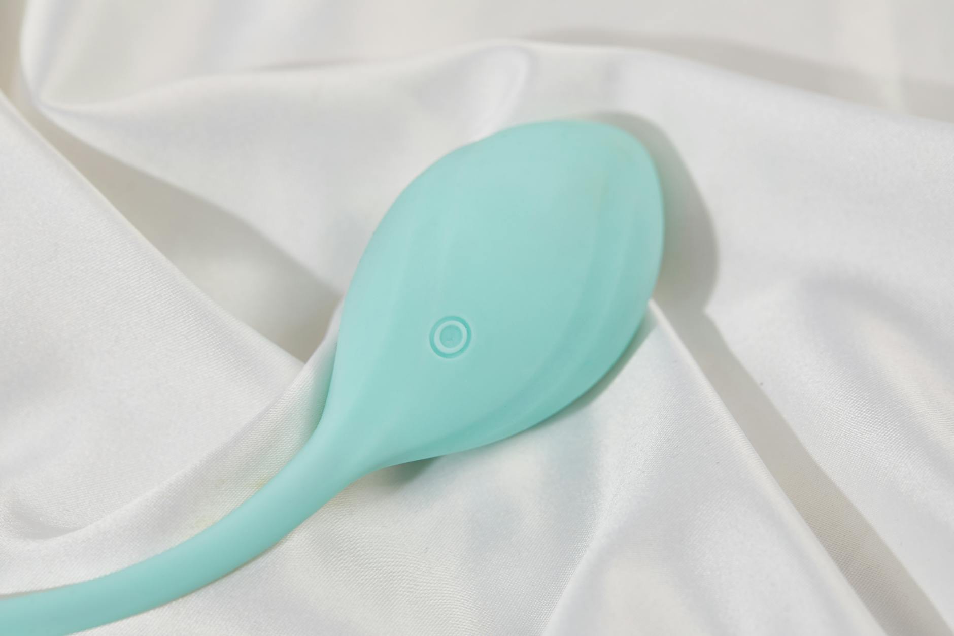 Teal vibrator on soft white silk fabric representing postpartum self-care and intimacy recovery