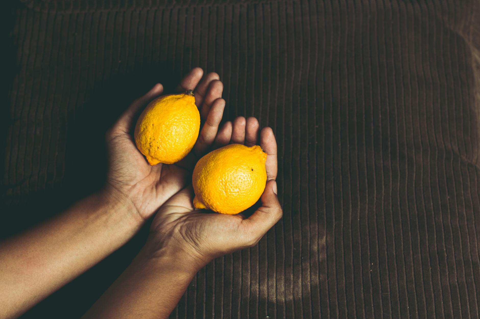 Close-up of two fresh lemons held in cupped hands, symbolizing connection and freshness.