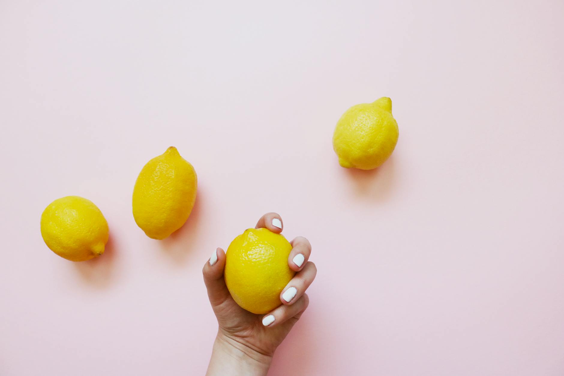Hands holding fresh lemons on a soft pink background, symbolizing gentle recovery and renewal