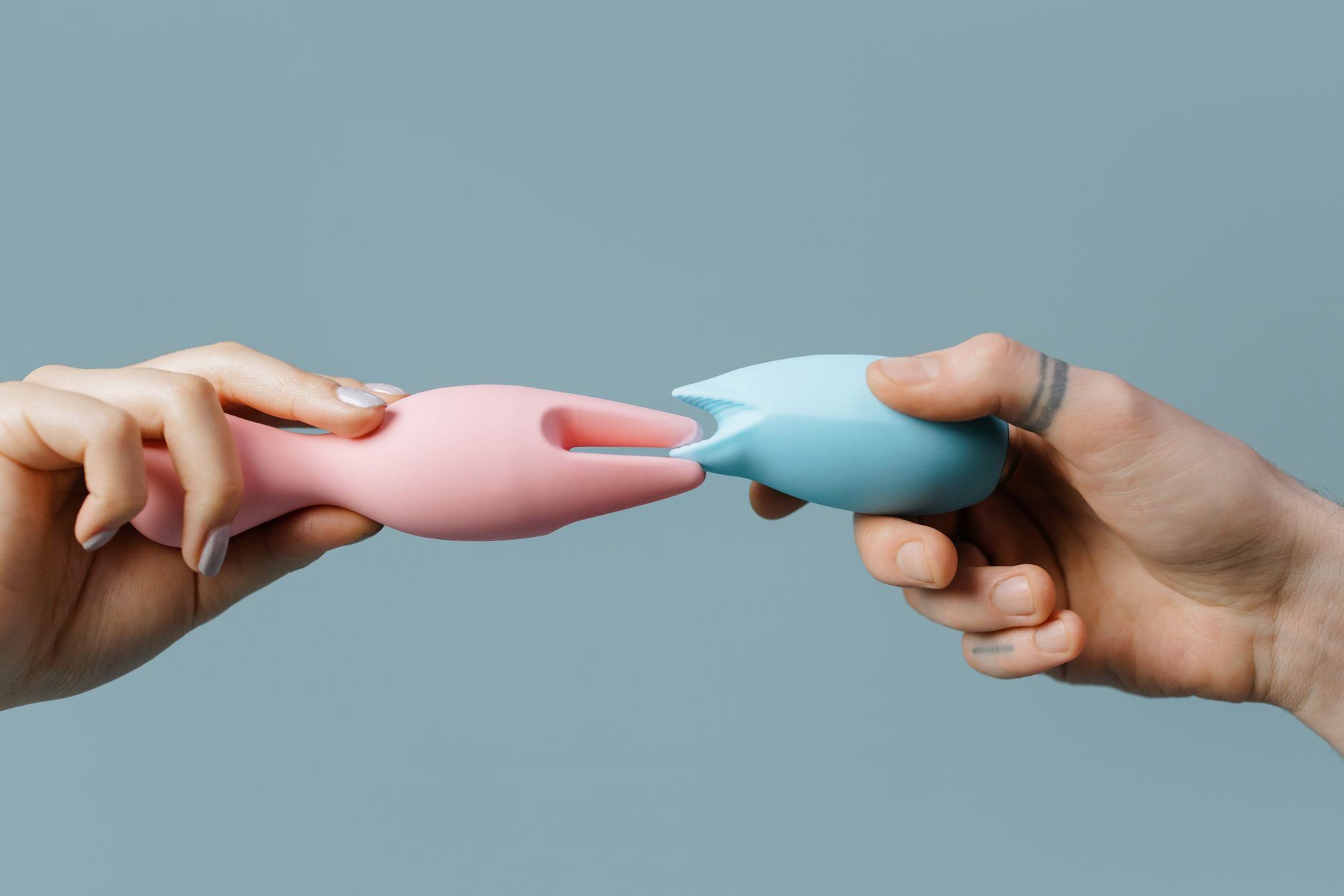 Mani che tengono vibratori colorati in silicone su sfondo neutro