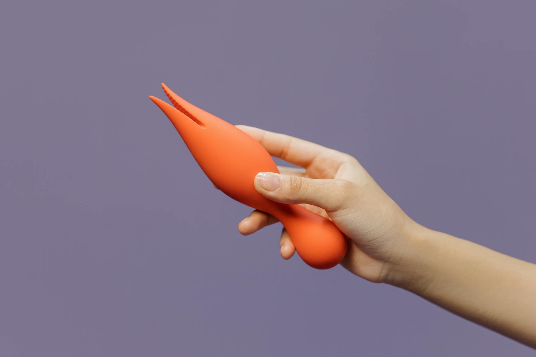 Un primo piano di mani che stringono un vibratore blu contro uno sfondo viola, che rappresenta l'intimità moderna.