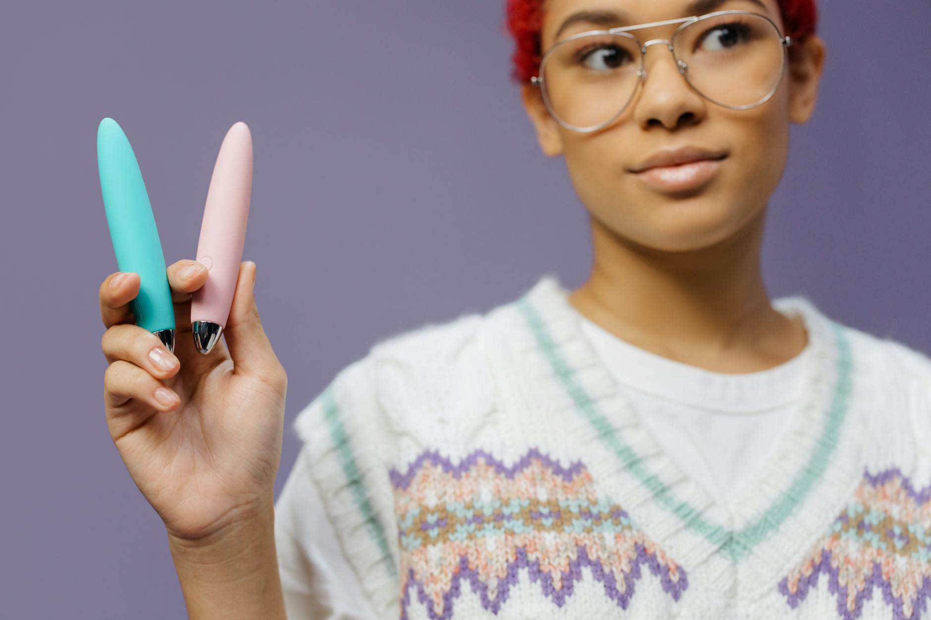 Woman holding blue and pink clitoral vibrators in a thoughtful moment of self-discovery