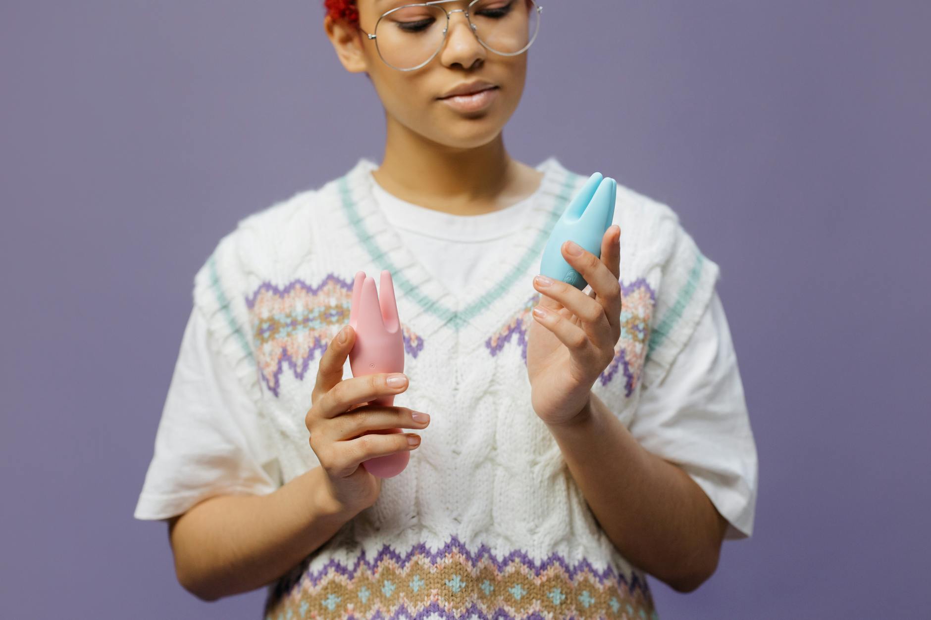 Woman holding blue and pink silicone lemon vibrators in thoughtful contemplation