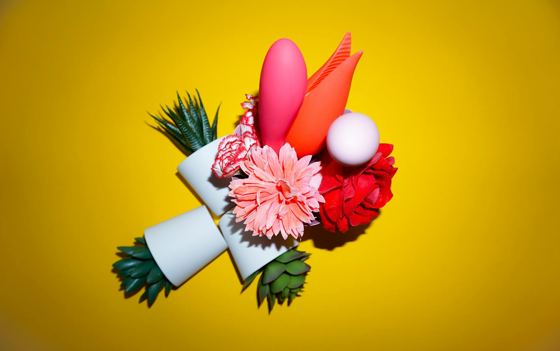 Woman holding lemon-colored and pink vibrators with thoughtful expression against neutral background