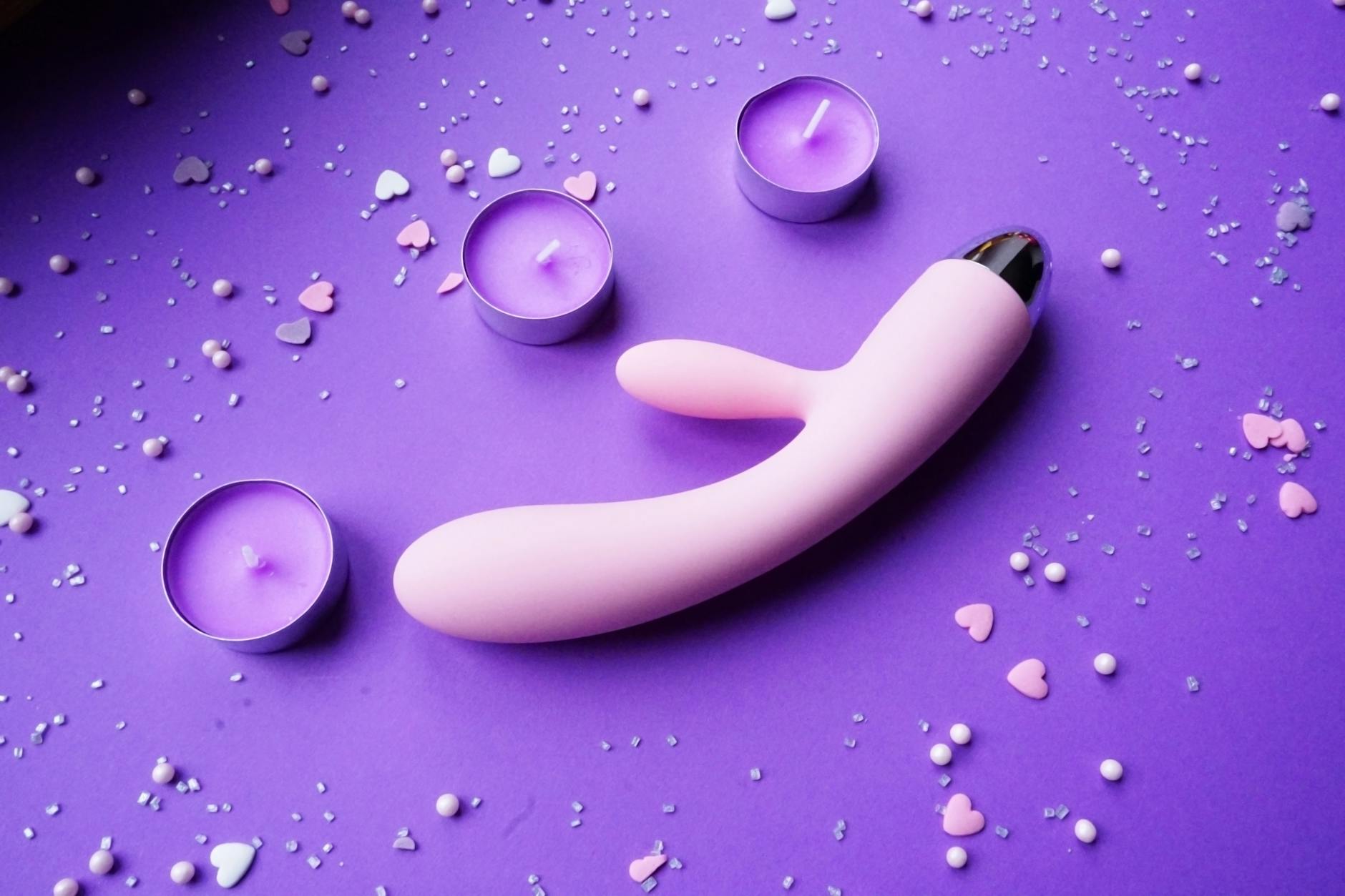 Vibratore rosa su sfondo viola con decorazioni a cuore e candele per un'atmosfera romantica